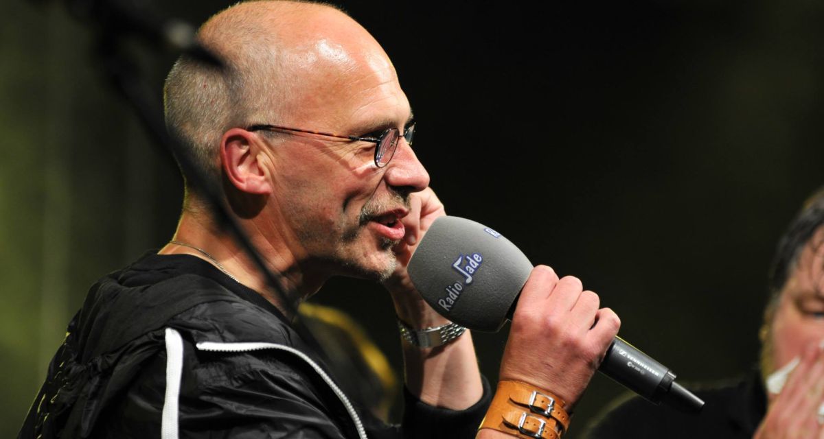 Zu sehen ist ein Mann, der ein Radio Jade Mikrofon hält und darin rein spricht.