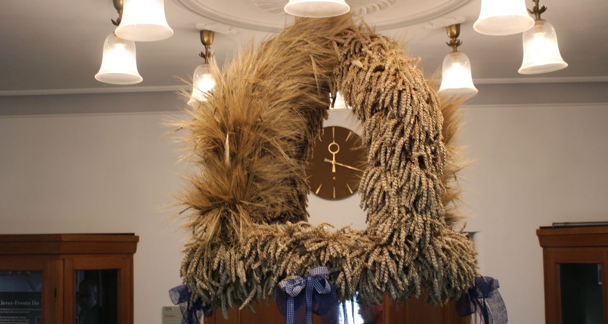 Zu sehen ist eine hängende Erntekrone, die mit Schleifen geschmückt ist. 