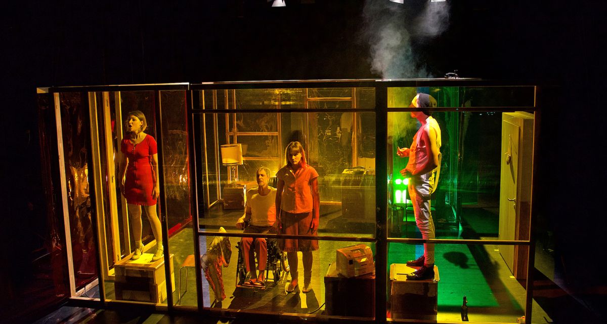 Auf einer Bühne stehen mehrere Menschen hinter bunten Folien. Drei schauen ins Publikum, einer raucht. Es ist das Bühnenbild von