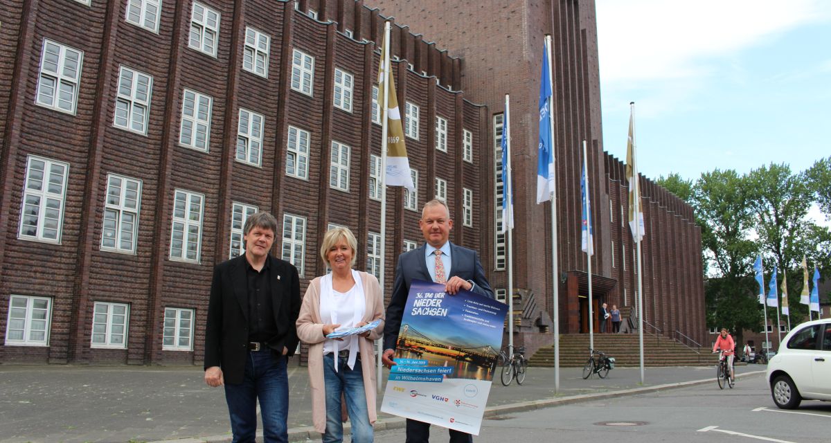 Michael Diers, Regina von Ewegen und Andreas Wagner stehen vor dem Rathaus. Sie halten Flyer und Plakate zum Tag der Niedersachsen in der Hand