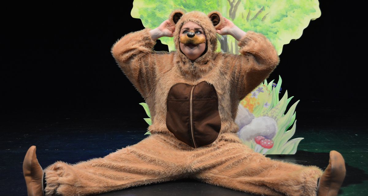 Eine Schauspielerin in einem Bärenkostüm sitzt auf einer Bühne.