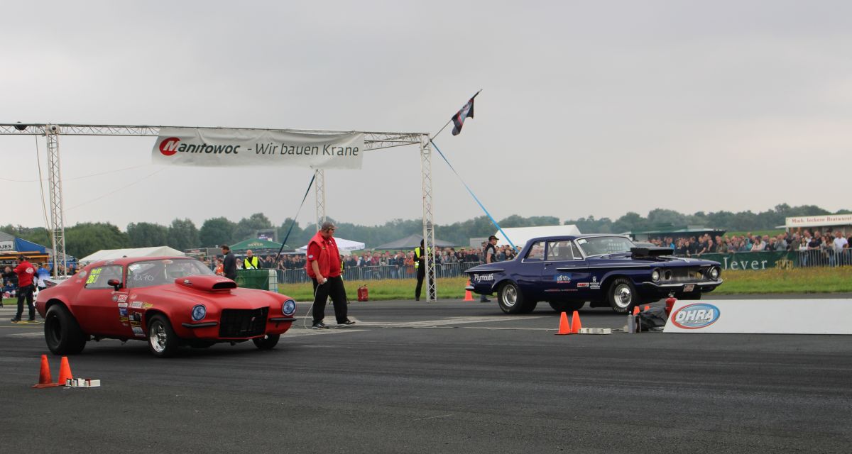 Ein rotes und ein blaues Auto warten auf ihr Startsignal beim Jade Race. Ein Streckenposten steht zwischen ihnen, im Hintergrund sind Zuschauer zu sehen