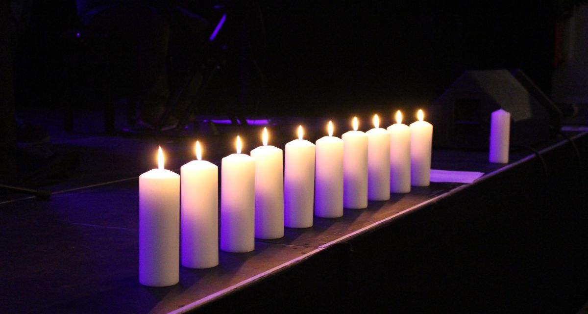 Auf dem Bild sind zehn entzündete, weiße Kerzen in einer Reihe zu sehen.