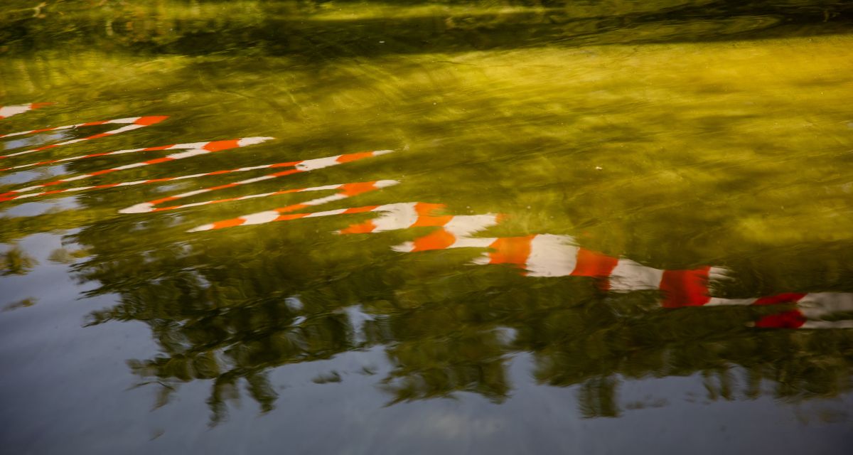 Zu sehen ist Wasser, in dem sich ein Absperrband spiegelt.