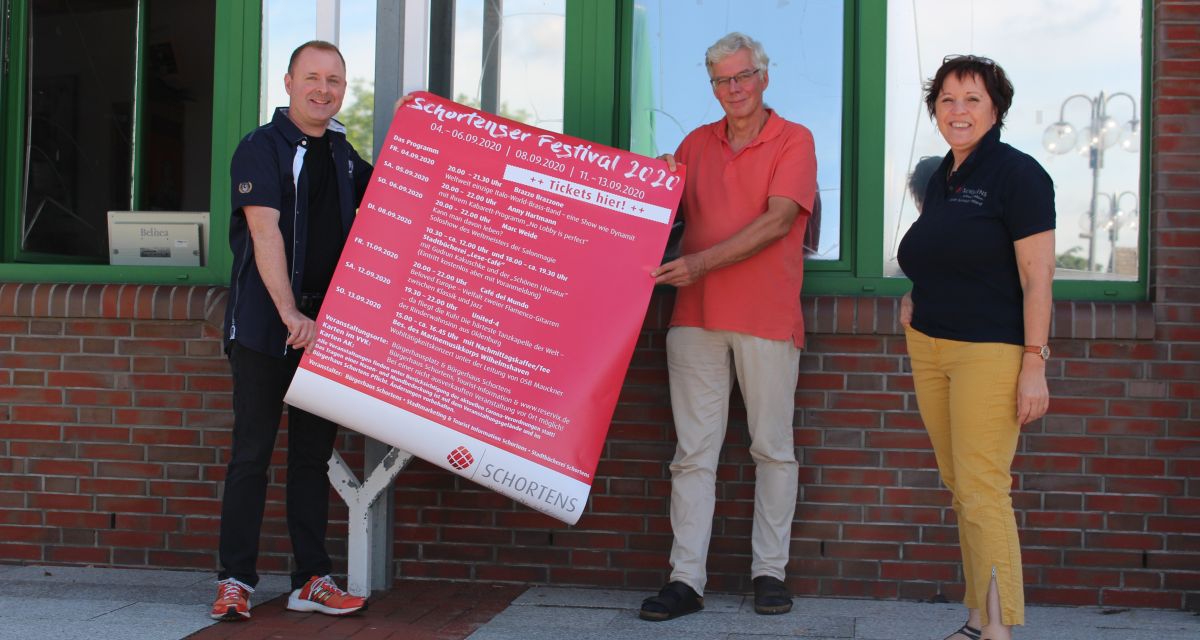 Die Veranstalter*innen des Schortenser Festivals stehen vor einer Wand und präsentieren das Plakat mit dem Programm