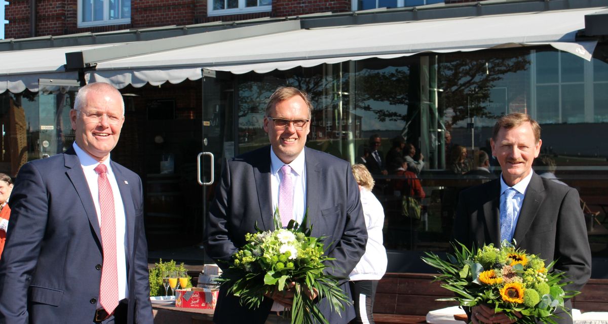 Drei Männer stehen vor einem Restaurant, während der neue Geschäftsführer der GPS vorgestellt wird. Von links nach recht sind dort Herr Flinks, Herr Puschmann und Herr Hoffmann zu sehen.