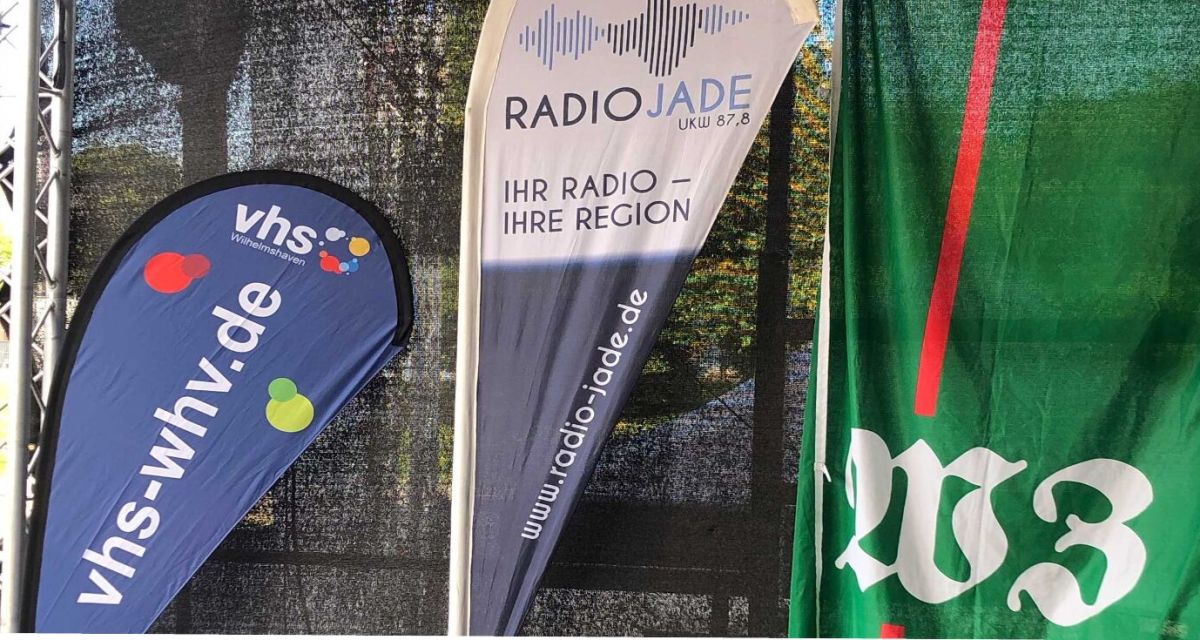 Zu sehen sind Beachflags mit Logo: Volkshochschule, Radio Jade, Wilhelmshavener Zeitung
