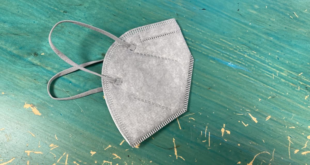 Auf dem Foto ist eine graue Mund-Nasen-Bedeckung vom Typ FFP zu sehen. Die Maske liegt auf einem türkisfarbenen Tisch.