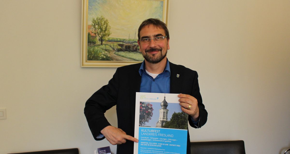 Frieslands Landrat Sven Ambrosy hält ein Plakat für das Kulturfest des Landkreises Friesland.