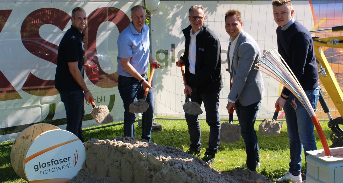 Spatenstich für den Glasfaserausbau in Hooksiel. Vertreter von Stadt und Betreibergesellschaft stehen mit Spaten in der Hand vor einem Transparent.