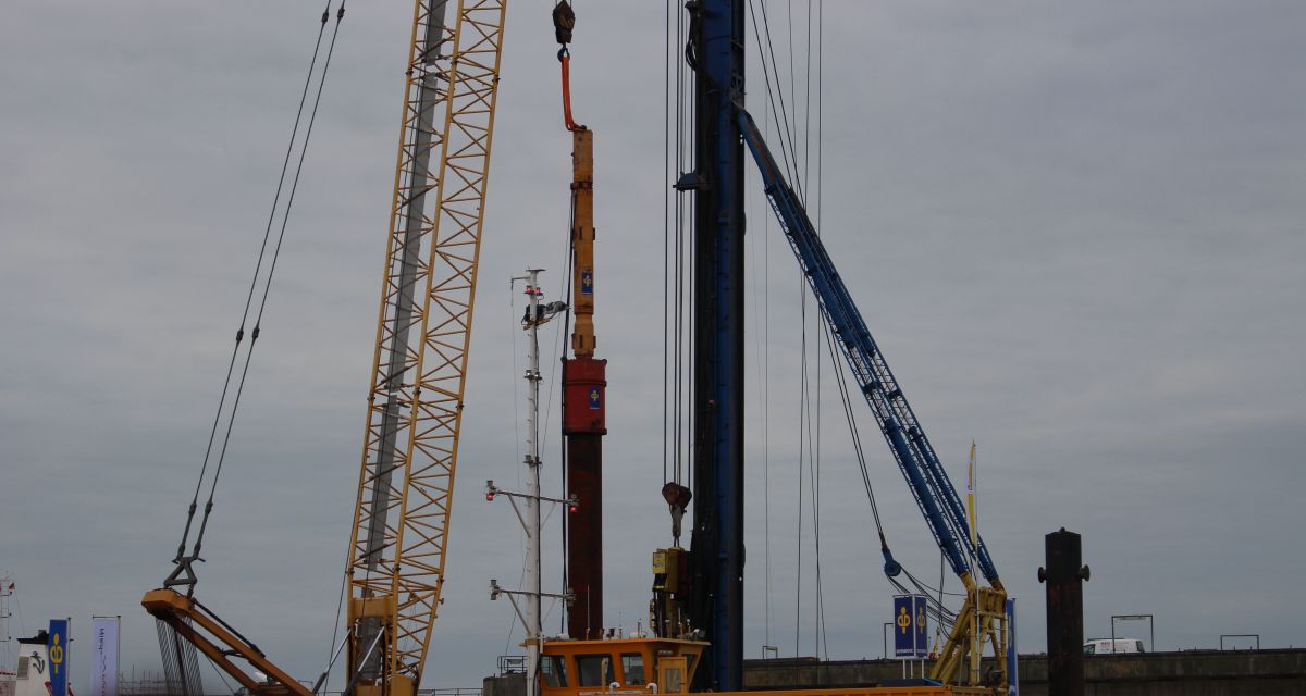 Der erste Rammschlag für das LNG-Terminal in Hooksiel, die Maschinen sind vor grauem Himmel zu sehen
