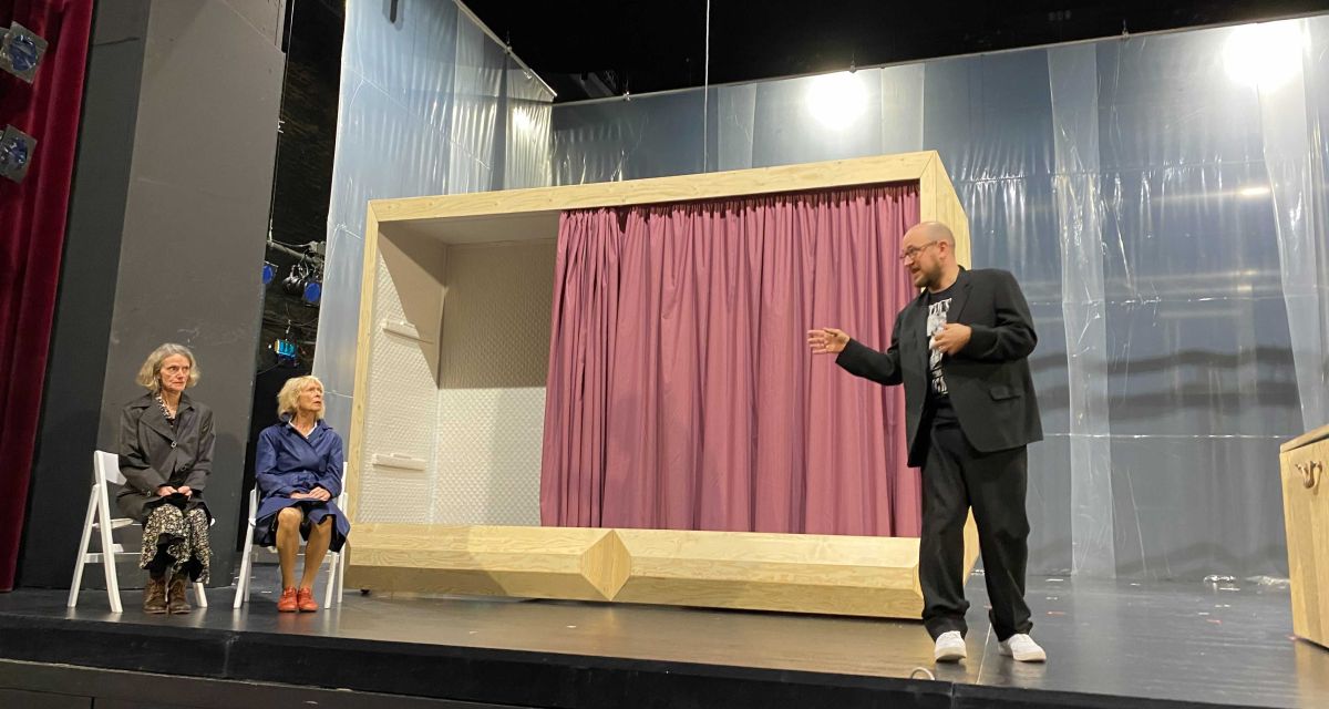 Drei Schauspieler*innen stehen und sitzen auf der Bühne im Stadttheater Wilhelmshaven. Sie proben das Stück