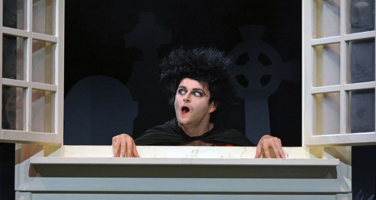 Der kleine Vampir schaut geschminkt durch ein geöffnetes Fenster in einen Raum.