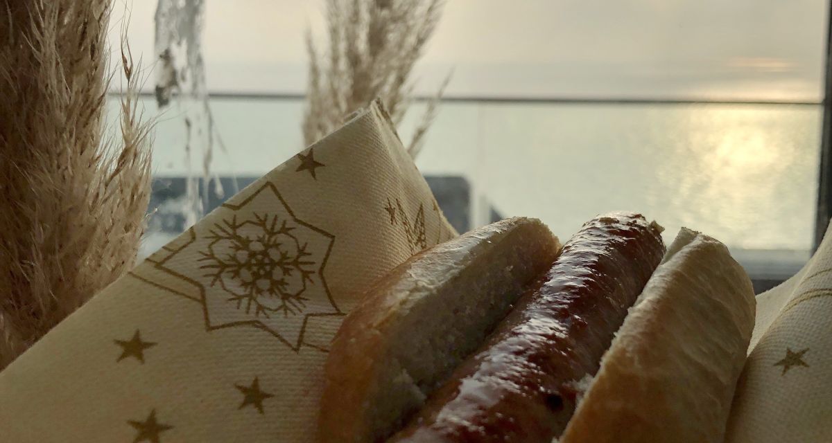 Eine Bratwurst aus Lammfleisch im Brötchen, dahinter das Meer