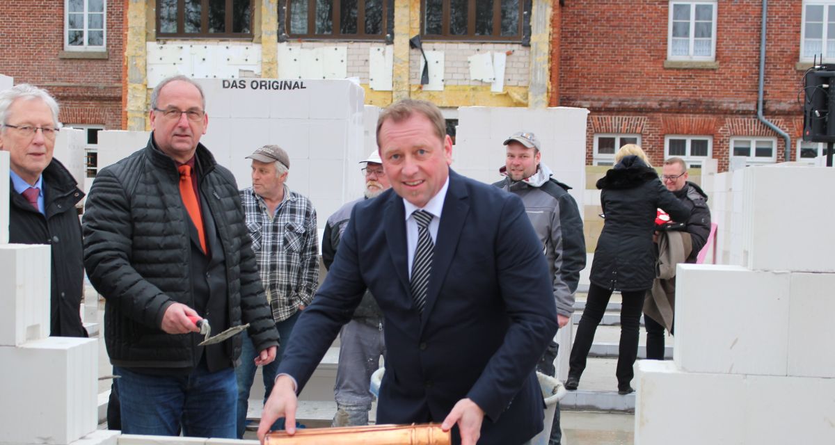 Bei der Grundsteinlegung für das neue Rathaus in Friedeburg lässt Bürgermeister Helfried Goetz eine Zeitkapsel in eine zur Hälfte hochgezogene Mauer.
