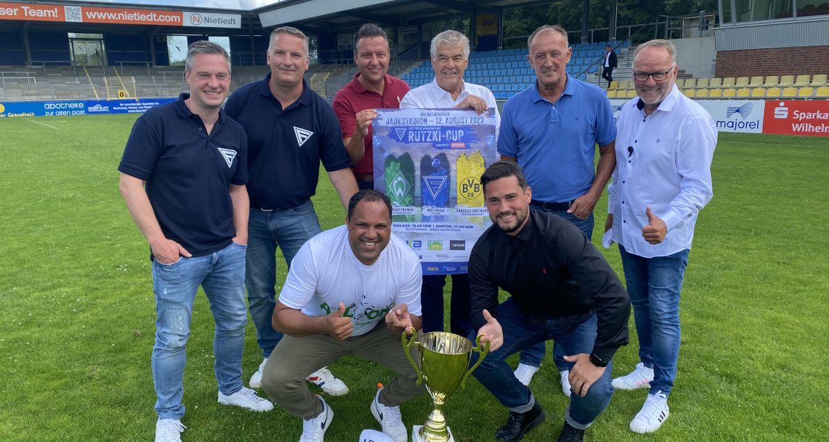 Die Organisatoren des Legendenturniers beim WSC Frisia posieren auf dem Platz mit einem Pokal