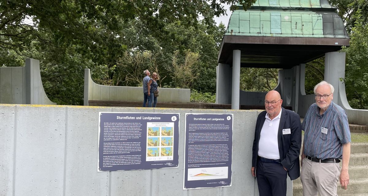 Heiner Holzhausen und Rainer Beckershaus stehen vor neu angebrachten Tafel am Rüstringer Berg in Wilhelmshaven