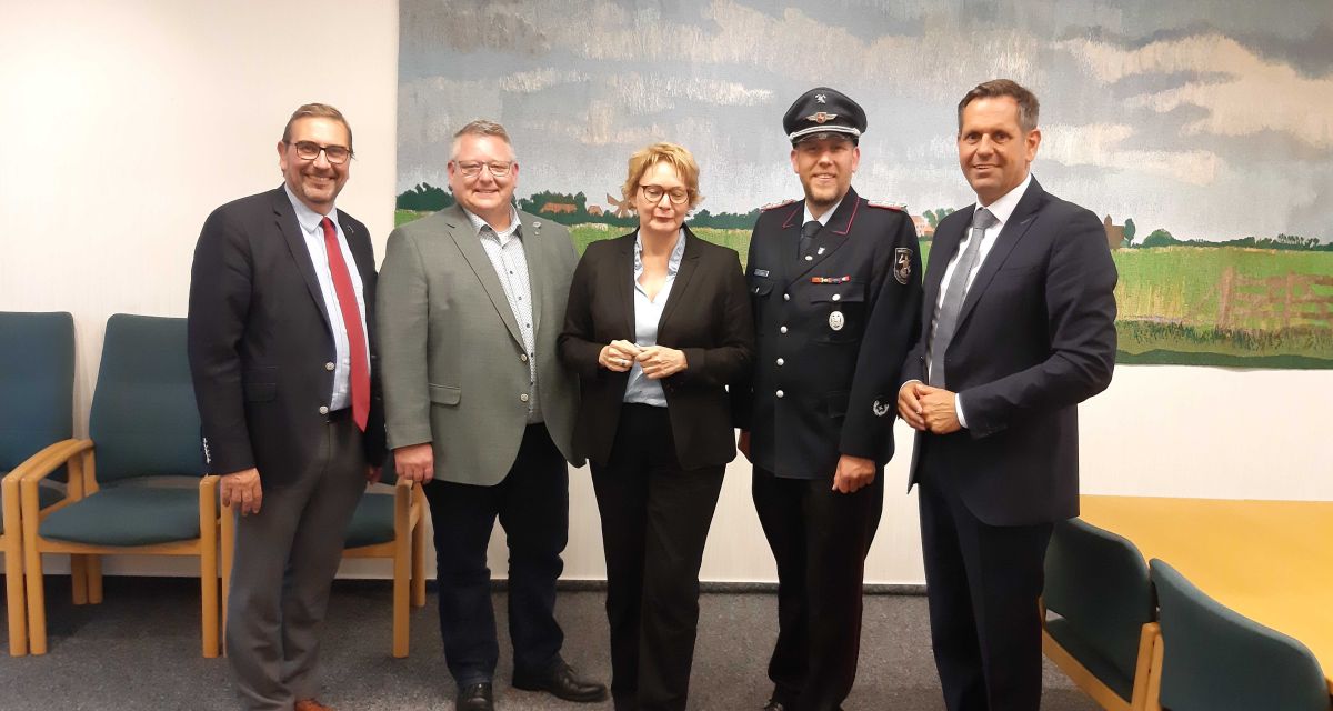 Frieslands Landrat Sven Ambrosy, der Bürgermeister der Gemeinde Wangerland Mario Szlezak, die niedersächsischen Minister*innen für Inneres und Wirtschaft Daniela Behrens und Olaf Lies, sowie ein Vertreter der Feuerwehr stehen für ein Gruppenfoto anlässlich von Besprechungen zum Katastrophenschutz in Hohenkirchen zusammen.