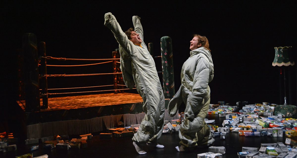 Szenenbild aus Nachts bevor die Sonne aufgeht. Simon Ahlborn und Anne Weise stehen auf der Bühne vor einem Boxring. Um sie herum liegen viele Tetrapacks.