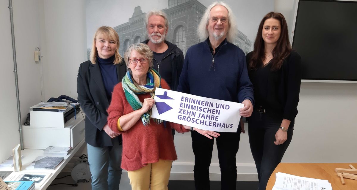 Der Arbeitskreis Gröschlerhaus stellt das Programm zum 10-jährigen Jubiläum vor. Fünf Menschen stehen mit dem Banner der Veranstaltung vor einer historischen Fotografie der jeverschen Synagoge