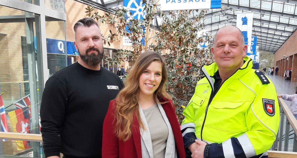 Die Zusammenarbeit der Polizei mit der Nordsee-Passage in Wilhelmshaven zur Stärkung des Sicherheitsgefühls wird vorgestellt. Zu sehen sind ein Mitarbeiter des Sicherheitsdienstes in schwarzer Dienstkleidung, Nadine Ennen vom Center-Management und Polizeihauptkommissar Tim Bachem in gelber Polizei-Warnweste. Sie lehnen am Geländer des Obergeschosses der Passage.