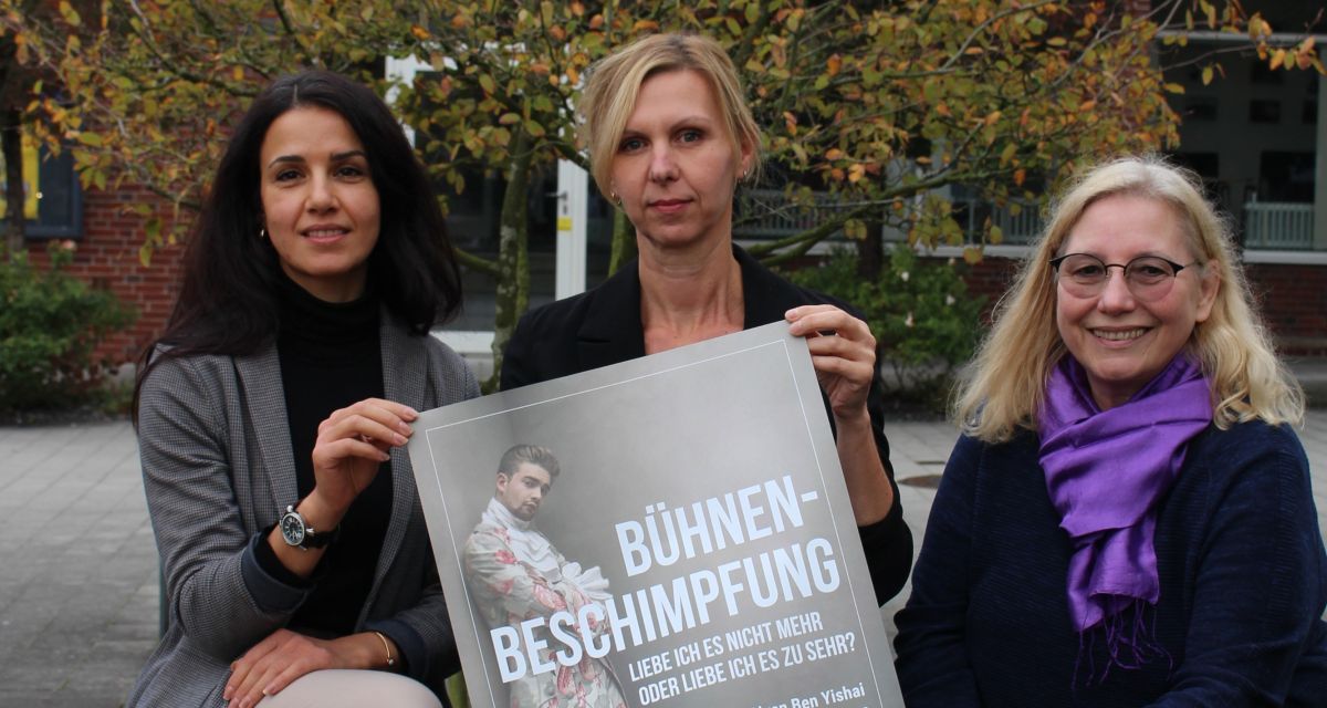 Zu sehen sind drei Frauen auf einer Bank: Sarah Helmy,Diana Bogdanski und Angelika Heinich. Sie halten ein Plakat der Landesbühne, auf dem für die Vorstellung