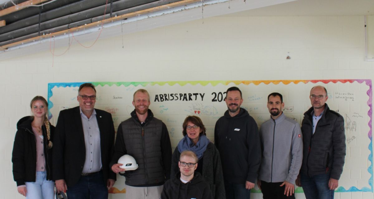 Auf dem Foto sieht man eine Gruppe Menschen vor einer Wand mit dem Graffiti