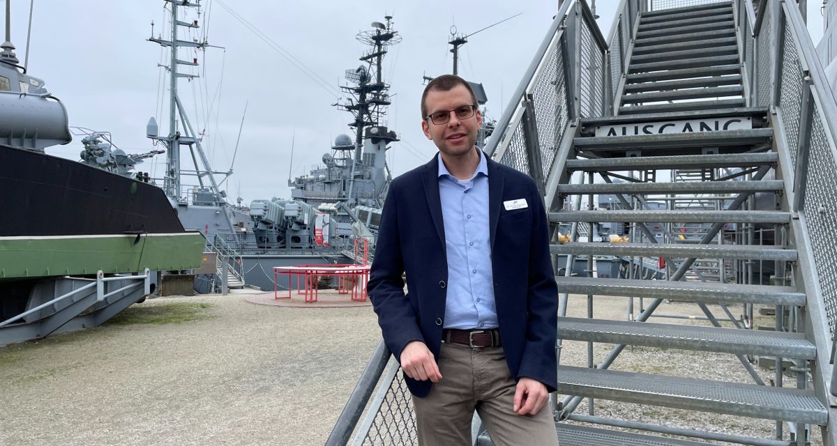 Zu sehen ist ein Mann in Bürokleidung im Freien auf einer Eisentreppe