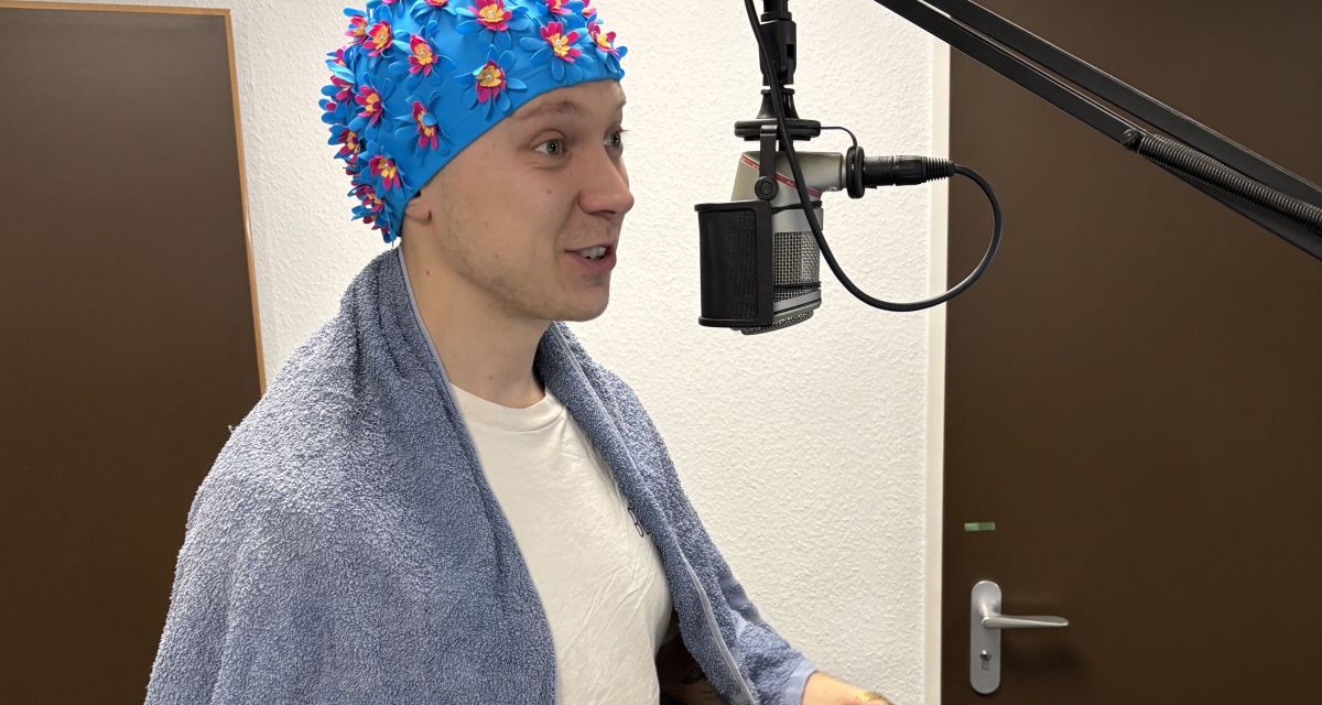 Ein Mann mit Handtuch und und Badekappe im Rundfunkstudio