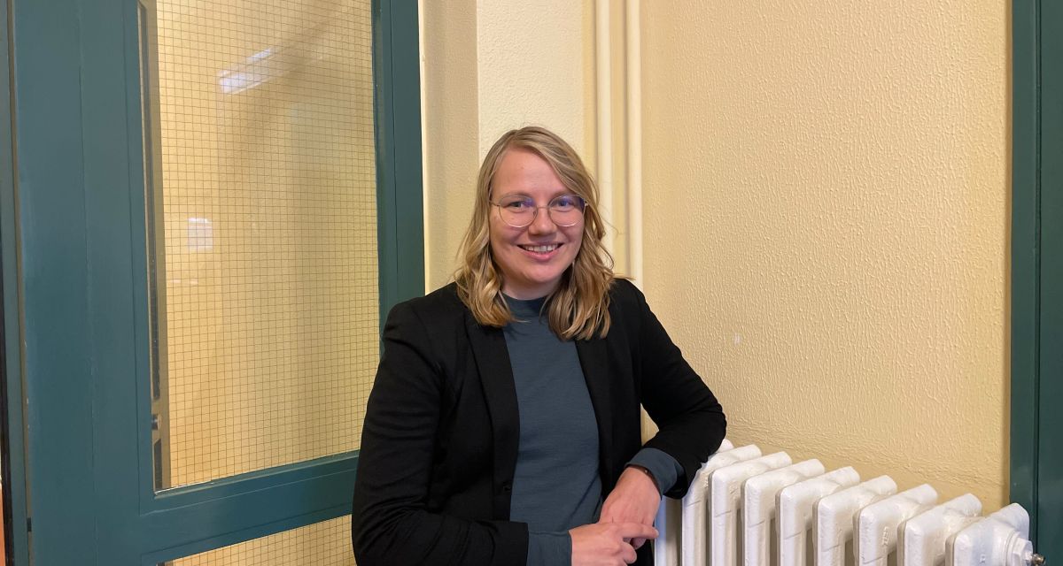 Die Klimaschutzmanagerin der Stadt Wilhelmshaven, Anne Jurack, steht an einen Heizkörper gelehnt vor einer petrolfarbenen Durchgangstür im Rathaus.
