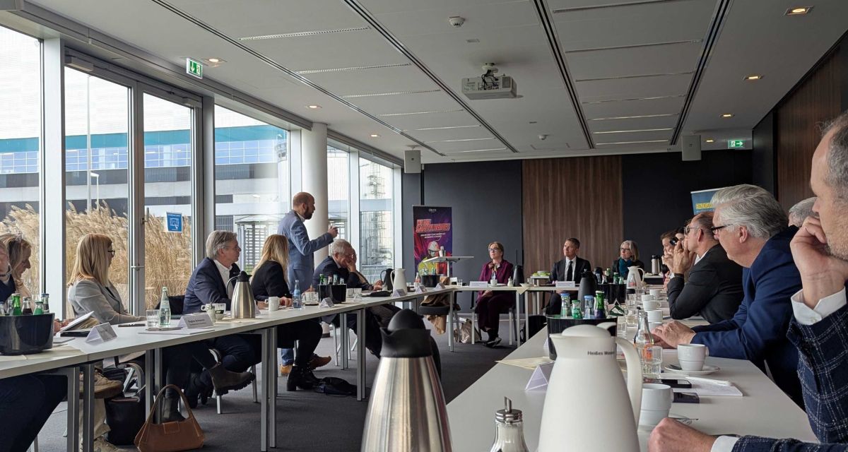 Teilnehmer*innen des Wirtschaftsdialogs in Wilhelmshaven sitzen in einem Besprechungsraum an Tischen. Am Dialog auf des Arbeitgeber- und Wirtschaftsverbandes Jade und des Energy Hub Port of Wilhelmshaven nahmen auf Einladung der SPD-Bundestagsabgeordneten Siemtje Möller auch de Botschafter*innen von Norwegen und Großbritannien teil. Die Teilnehmer*innen haben Notizzettel vor sich, auf den Tischen stehen Tee- und Kaffeekannen und -tassen. Uwe Opitz, Sprecher des Energy Hubs steht und spricht zu den Teilnehmer*innen.