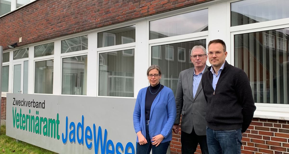 Auf dem Foto stehen (von links) Dr. Melanie Schweizer (Verbandsgeschäftsführerin), Bernd Niebuhr (Vorsitzender der Verbandsversammlung) und Dr. Michael Bucher (stellvertretender Verbandsgeschäftsführer) vor dem Schild des Zweckverbandes Veterinäramt JadeWeser. 