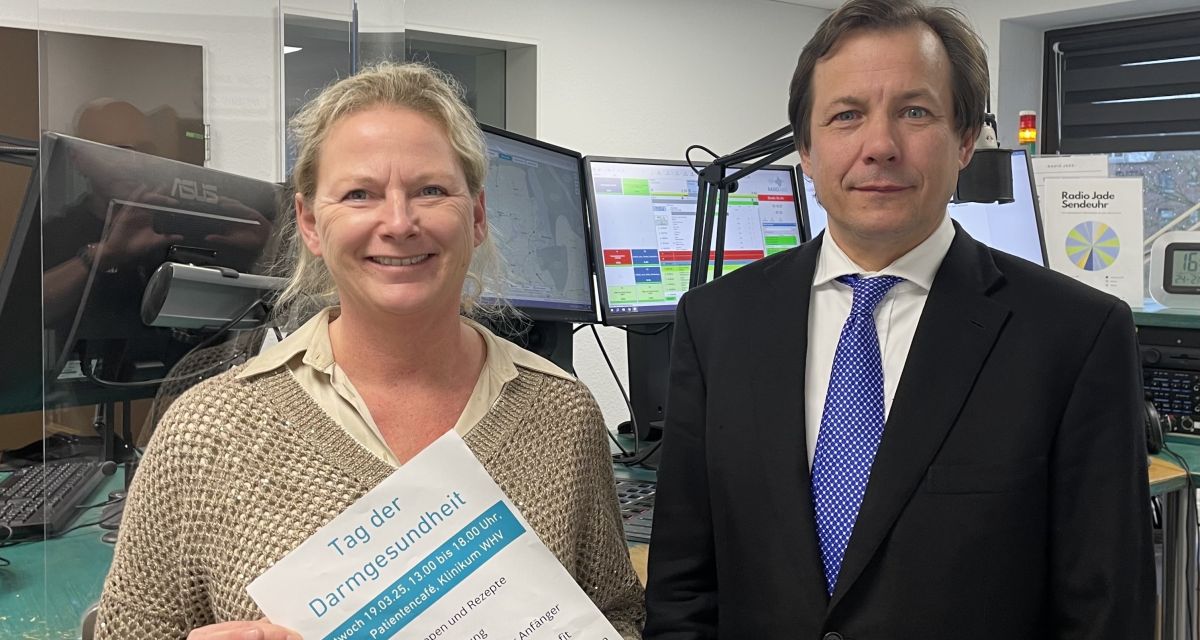 Zu sehen sind ein Mann und eine Frau im Studio, einen Flyer haltend