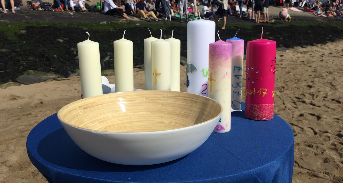 Zu sehen sind kirchliche Kerzen und eine Taufschüssel bei der Südstrandtaufe im Jahr 2017.