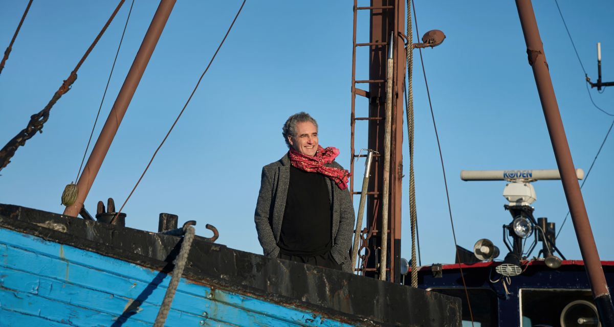 Der künstlerische Leiter der Gezeitenkonzerte der Ostfriesischen Landschaft, Matthias Kirschnereit. Er steht an Bord eines blauen Segelbootes.