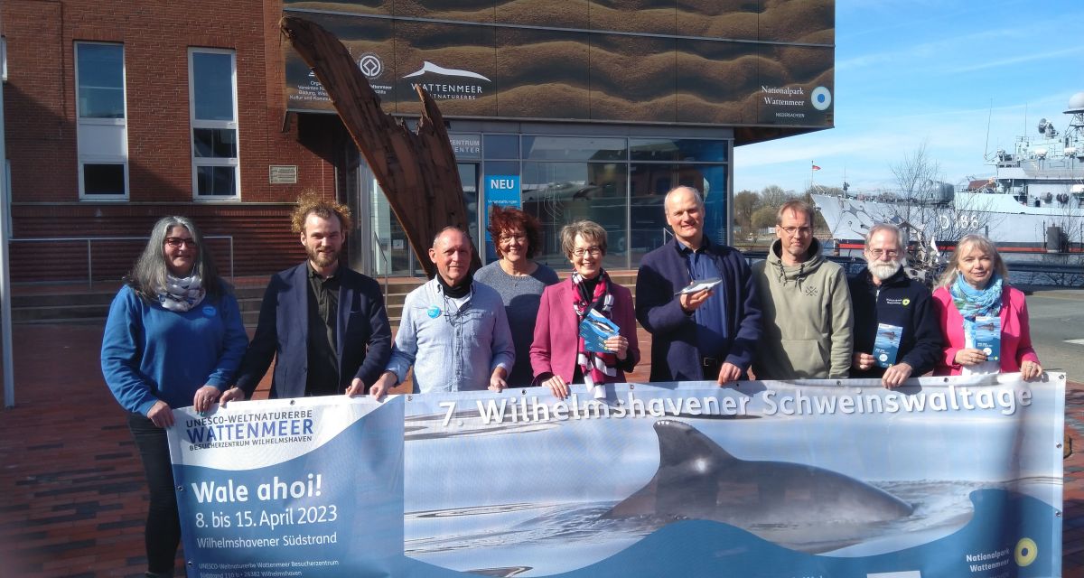 Zu sehen sind mehrere Menschen, die ein Banner der siebten Wilhelmshavener Schweinswaltage halten. 