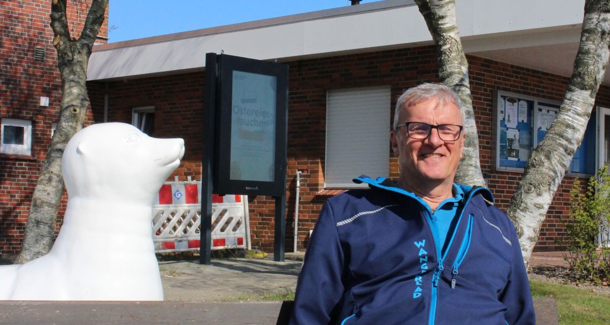 Zu sehen ist Ingo Kruse, Leiter des Campingplatz Schillig. Er sitzt auf einer Bank vor der Rezeption des Campingplatzes in der Sonne.