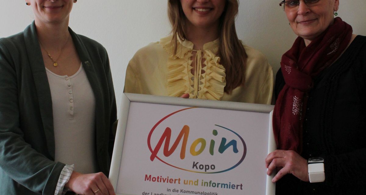 Zu sehen sind Ann-Catrin Cramer, Tomma Siebels und Nicole Biela. Sie halten ein Schild vom Projekt MOIN Kopo.