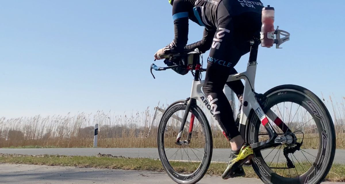Zu sehen ist ein behelmter Radfahrer in funktionaler Ausstattung auf dem Weg nach links, ein Windrad passierend