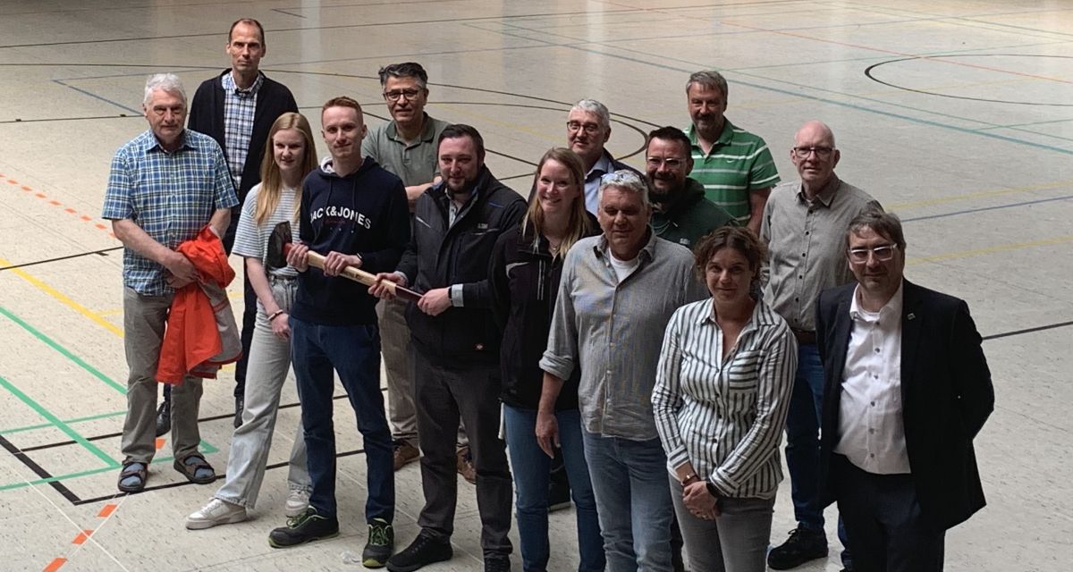 Auf dem Foto sind Vertreter*innen der Oberschule Hohenkirchen, der Baufirmen, des KreisSportBundes Friesland und des Landkreises Friesland, unter anderem Landrat Sven Ambrosy, zu sehen. Sie stehen in der zu sanierenden Sporthalle.