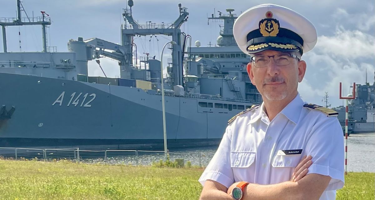 Zu sehen ist Andreas Schmekel, Kapitän zur See und Kommandant des Trossgeschwaders in Uniform vor dem Einsatzgruppenversorger Frankfurt am Main