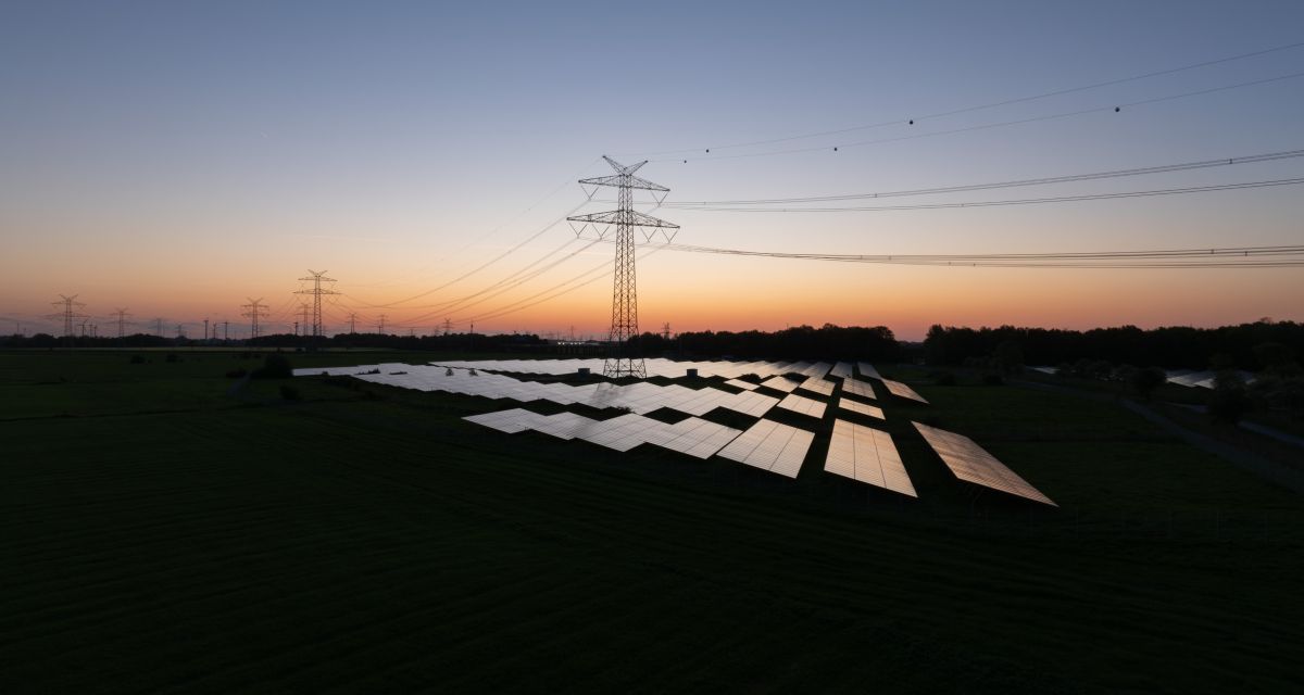 Zu sehen ist ein Solarpak mit hochstpannungsleitungen in der Dämmerung