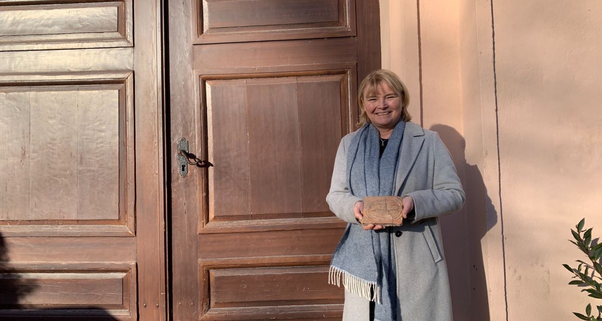 Zu sehen ist Dr. Antje Sander, Leiterin des Schlossmuseums Jever. Das Museum hat einen Rückblick für das Jahr 2025 und einen Ausblick für das Jahr 2026 gegeben. Bei Arbeiten im Schlosspark wurde eine mittelalterliche Fliese gefunden, die einen laufenden Hasen zeigt. Mit dieser Fliese steht Antje Sander vor dem Schlossmuseum.