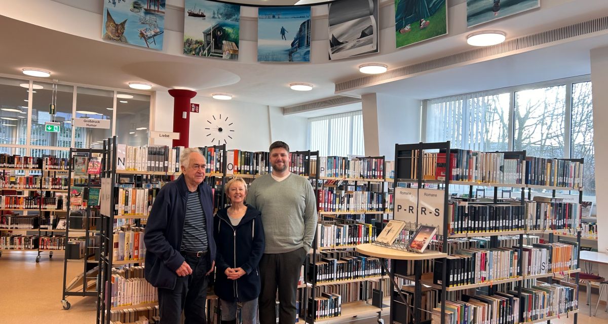 Zu sehen sind unter sechs großformatigen Bildern im Saal der Wilhelmshavener Stadtbibliothek der Künstler Hartmut Wiesner, die Bibliothekarin Andrea Felsch und der Bibliotheksleiter Helge Ralle