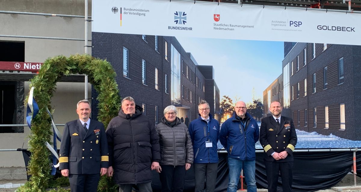 Am 10. Februar 2026 konnte das Richtfest für elf neue Unterkunftsgebäude auf der Norderweiterung des Marinestützpunktes in Wilhelmshaven gefeiert werden. Einige der Verantwortlichen stehen vor einem Projektplakat und der Richtkrone.
Von links: Kapitän zur See Hanno Weisensee (Referatsleiter im Bundesamt für Infrastruktur, Umweltschutz und Dienstleistungen der Bundeswehr), Oberbürgermeister Carsten Feist, Sabine Tegtmeyer-Dette (Staatssekretärin im Niedersächsischen Finanzministerium), Alexander Schaub (Leiter des Staatlichen Baumanagements in Hannover), Jörn Tacke (Projektleiter, Staatliches Baumanagement) und Fregattenkapitän Volker Kübsch.