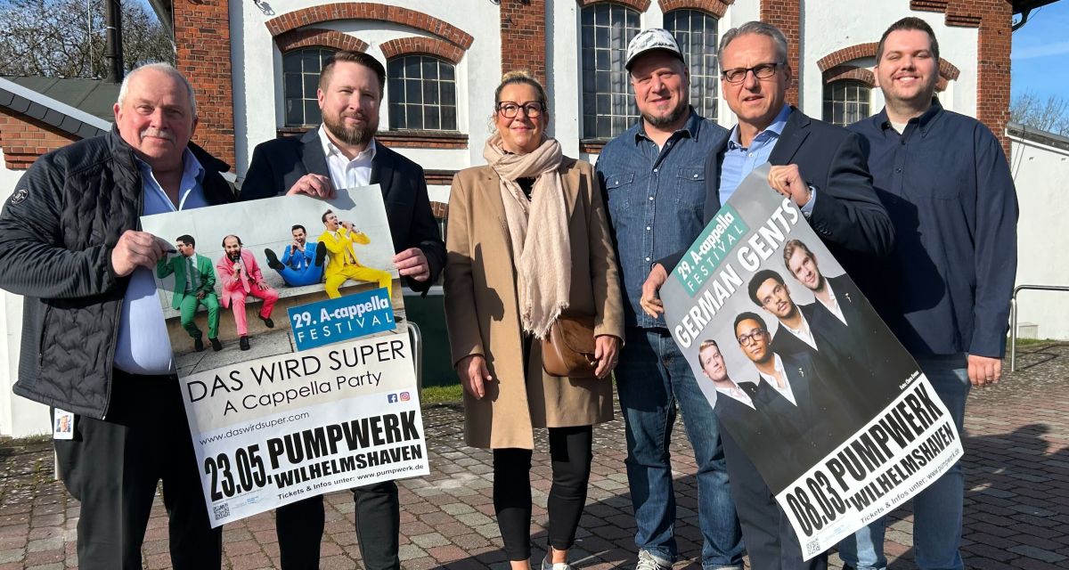 Am Kulturzentrum Pumpwerk in Wilhelmshaven wird das Programm des 29. A-cappella-Festival vorgestellt. Von links nach rechts stehen Ulf Timmermann, Daniel Schnitger, Wiebke Babatz, Mirco Wenzel, Matthias Witte und Tom Rakow mt zwei Plakaten der Veranstaltungsreihe vor dem Pumpwerk.