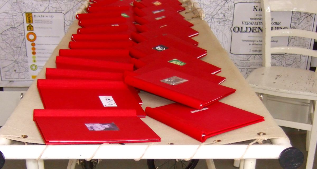 Zu sehen sind etwa 20 rote mappen auf einem Tisch vor einer Wandkarte. Sie beiinhalten die geschichten von Euthanasieopfern.