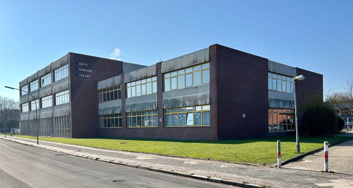 Zu sehen ist eine kantiger Sechszigerjahre Schulbau mit gelben Fensterrahmen von der Straßenseite