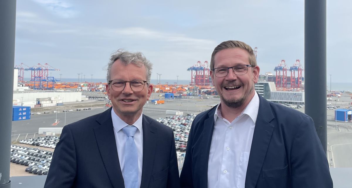 Zu sehen sind zwei Männer vor Hafenkulisse