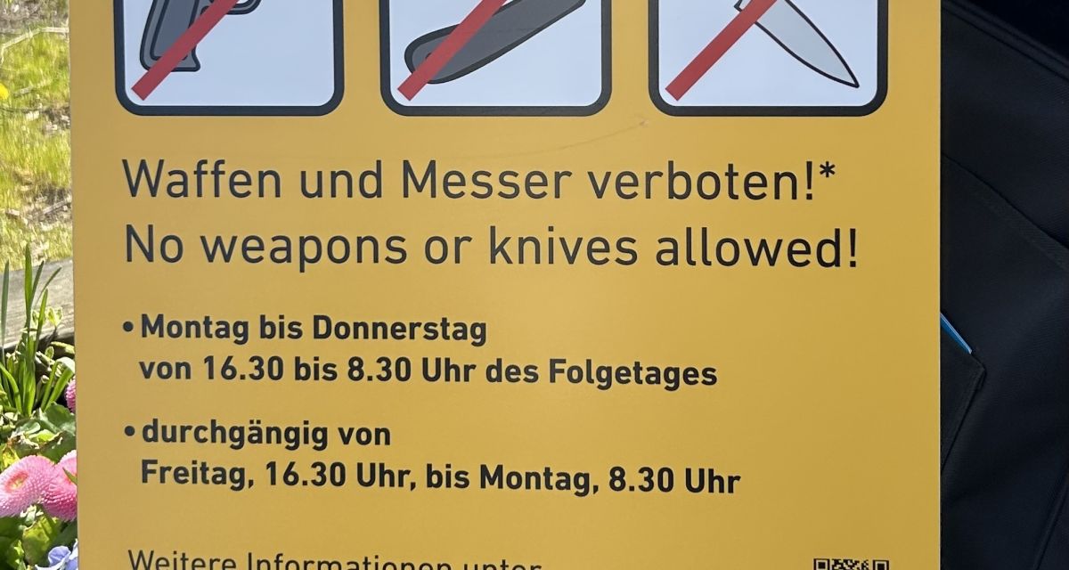 Zu sehen ist ein Schild zur Kennzeichnung einer Waffenverbotszone mit Schrift, Piktogrammen und einem QR-Code